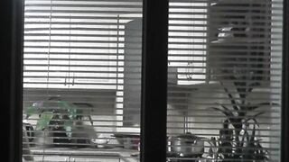 Peeping. Voyeur. Neighbors pervert voyeur inside evening on street looks out window as nude beauty neighbors inside kitchen prepares dinner for her hubby. Nude into outdoor. Nude at home. Family. Public