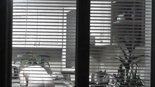 Peeping. Voyeur. Neighbors pervert voyeur inside evening on street looks out window as nude beauty neighbors inside kitchen prepares dinner for her hubby. Nude into outdoor. Nude at home. Family. Public