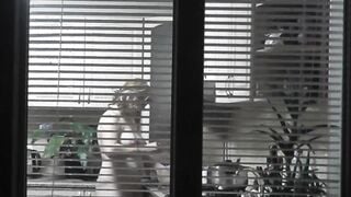 Peeping. Voyeur. Neighbors pervert voyeur inside evening on street looks out window as nude beauty neighbors inside kitchen prepares dinner for her hubby. Nude into outdoor. Nude at home. Family. Public