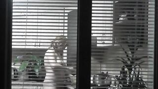Peeping. Voyeur. Neighbors pervert voyeur inside evening on street looks out window as nude beauty neighbors inside kitchen prepares dinner for her hubby. Nude into outdoor. Nude at home. Family. Public