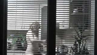 Peeping. Voyeur. Neighbors pervert voyeur inside evening on street looks out window as nude beauty neighbors inside kitchen prepares dinner for her hubby. Nude into outdoor. Nude at home. Family. Public