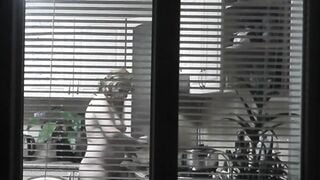 Peeping. Voyeur. Neighbors pervert voyeur inside evening on street looks out window as nude beauty neighbors inside kitchen prepares dinner for her hubby. Nude into outdoor. Nude at home. Family. Public