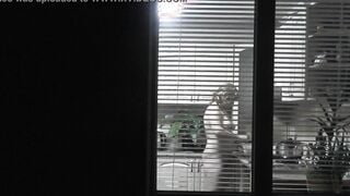 Peeping. Voyeur. Neighbors pervert voyeur inside evening on street looks out window as nude beauty neighbors inside kitchen prepares dinner for her hubby. Nude into outdoor. Nude at home. Family. Public