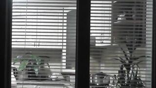Peeping. Voyeur. Neighbors pervert voyeur inside evening on street looks out window as nude beauty neighbors inside kitchen prepares dinner for her hubby. Nude into outdoor. Nude at home. Family. Public