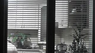 Peeping. Voyeur. Neighbors pervert voyeur inside evening on street looks out window as nude beauty neighbors inside kitchen prepares dinner for her hubby. Nude into outdoor. Nude at home. Family. Public