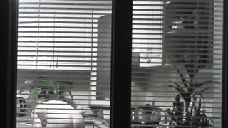 Peeping. Voyeur. Neighbors pervert voyeur inside evening on street looks out window as nude beauty neighbors inside kitchen prepares dinner for her hubby. Nude into outdoor. Nude at home. Family. Public