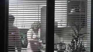 Peeping. Voyeur. Neighbors pervert voyeur inside evening on street looks out window as nude beauty neighbors inside kitchen prepares dinner for her hubby. Nude into outdoor. Nude at home. Family. Public
