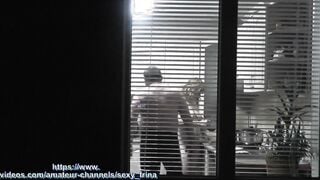 Peeping. Voyeur. Neighbors pervert voyeur inside evening on street looks out window as nude beauty neighbors inside kitchen prepares dinner for her hubby. Nude into outdoor. Nude at home. Family. Public