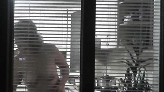 Peeping. Voyeur. Neighbors pervert voyeur inside evening on street looks out window as nude beauty neighbors inside kitchen prepares dinner for her hubby. Nude into outdoor. Nude at home. Family. Public
