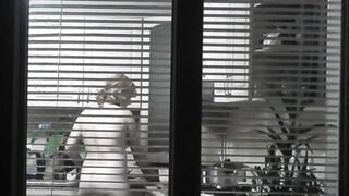 Peeping. Voyeur. Neighbors pervert voyeur inside evening on street looks out window as nude beauty neighbors inside kitchen prepares dinner for her hubby. Nude into outdoor. Nude at home. Family. Public