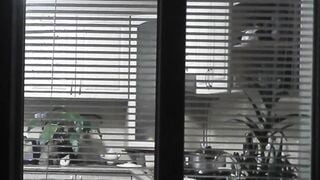 Peeping. Voyeur. Neighbors pervert voyeur inside evening on street looks out window as nude beauty neighbors inside kitchen prepares dinner for her hubby. Nude into outdoor. Nude at home. Family. Public