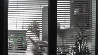 Peeping. Voyeur. Neighbors pervert voyeur inside evening on street looks out window as nude beauty neighbors inside kitchen prepares dinner for her hubby. Nude into outdoor. Nude at home. Family. Public