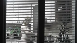 Peeping. Voyeur. Neighbors pervert voyeur inside evening on street looks out window as nude beauty neighbors inside kitchen prepares dinner for her hubby. Nude into outdoor. Nude at home. Family. Public