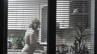 Peeping. Voyeur. Neighbors pervert voyeur inside evening on street looks out window as nude beauty neighbors inside kitchen prepares dinner for her hubby. Nude into outdoor. Nude at home. Family. Public
