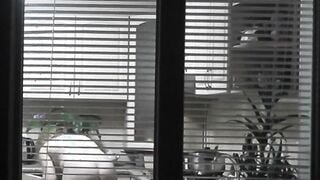 Peeping. Voyeur. Neighbors pervert voyeur inside evening on street looks out window as nude beauty neighbors inside kitchen prepares dinner for her hubby. Nude into outdoor. Nude at home. Family. Public