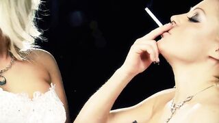 Playful blondes brush each other and kiss while holding cigarettes