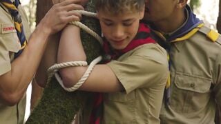 Scout boy bound up against a tree inside the woods by 2 mature scout boys